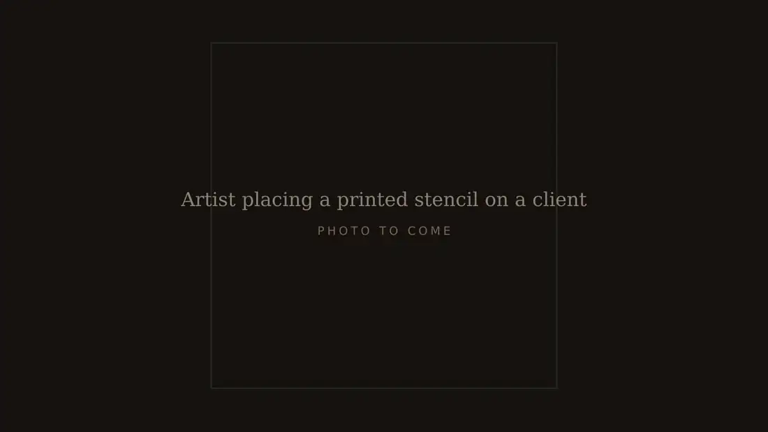 Artist placing a printed stencil on a client's inner forearm before a first tattoo